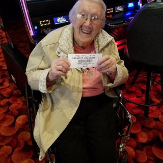 An elderly woman in a wheelchair holding a winning ticket at a casino.
