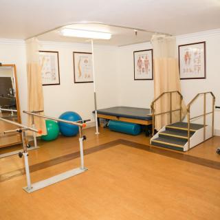 A physical therapy room equipped with parallel bars, exercise balls, and a small staircase for rehabilitation exercises.