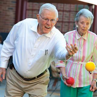 An elderly couple enjoying a game of bocce ball in the outdoors.