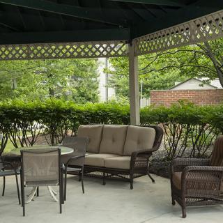 A cozy outdoor seating area under a gazebo, featuring comfortable chairs and a small table surrounded by greenery.