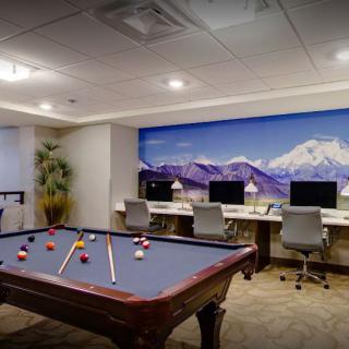 A modern game room featuring a pool table and computers, with a scenic mountain mural in the background.
