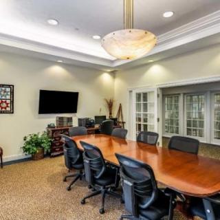 A well-lit conference room with a large wooden table surrounded by black office chairs.