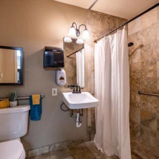 A clean and modern bathroom featuring a sink, toilet, mirror, and shower with a white curtain.