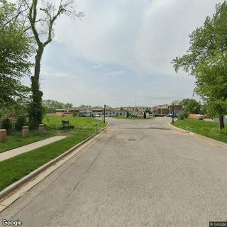 A quiet suburban street lined with trees and well-maintained lawns on a clear day.