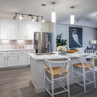 A modern kitchen featuring white cabinets, a central island with bar stools, pendant lighting, and stainless steel appliances.