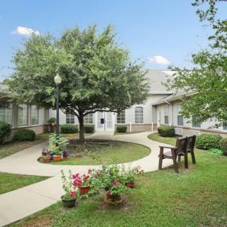 A peaceful garden area with pathways, benches, and trees surrounding a building.