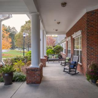A cozy porch with rocking chairs and plants, attached to a brick building.