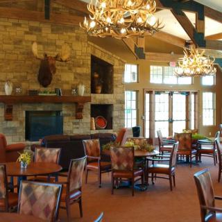 A rustic restaurant interior with a stone fireplace and antler chandeliers.