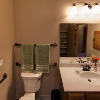 A well-lit bathroom featuring a toilet, sink with countertop, mirror, and neatly hung towels.