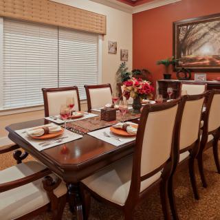A warmly lit dining room with a table set for a meal, featuring elegant chairs and tasteful decorations.