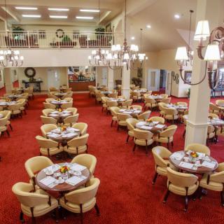 Spacious dining hall with elegant chandeliers and neatly arranged tables on a red carpeted floor.