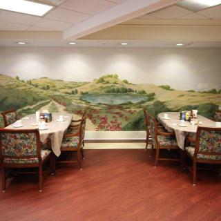 A cozy dining area with tables and chairs, featuring a large landscape mural on the wall.