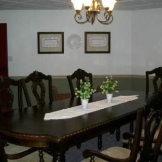 Elegant dining room with a large table and classic chairs, featuring decorative plants and a chandelier.