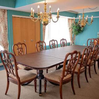An elegant dining room featuring a large wooden table surrounded by matching chairs, with chandeliers and draped curtains adding a touch of sophistication.