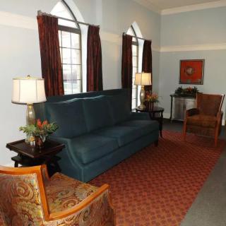 A cozy living room featuring a blue sofa, armchairs, and tall arched windows with red curtains.