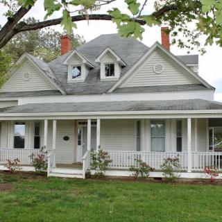 A charming Victorian-style house with a spacious front porch and a well-maintained lawn.