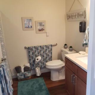 A neatly arranged bathroom with decorative elements, featuring a toilet, towels, wall art, and a rug.