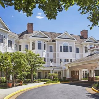 A large residential building with an entrance surrounded by trees under a clear blue sky.