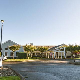A large, well-maintained building with a driveway and surrounding greenery under a clear sky.