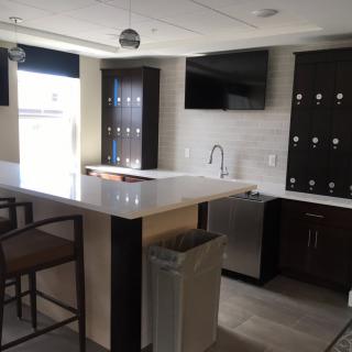 A modern kitchen with a sleek countertop and barstools, featuring dark cabinetry and built-in appliances.
