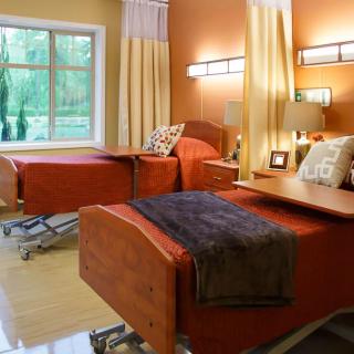 A hospital room with two patient beds, featuring a warm interior design and furniture.
