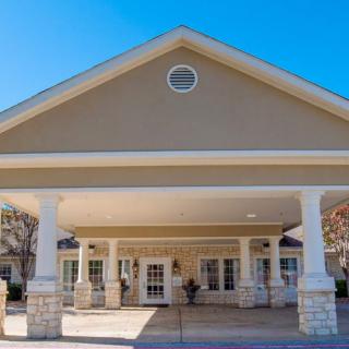 The image shows the front entrance of a building with a covered walkway supported by columns.