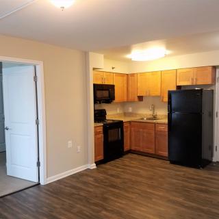 A modern apartment kitchen with wooden cabinets and black appliances.