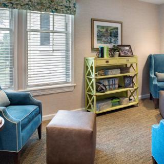 A cozy living room with colorful chairs, a bookshelf, and a window bringing in natural light.