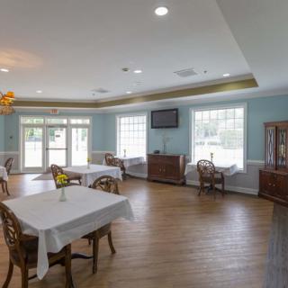 A spacious and bright dining room with neatly arranged tables and chairs, featuring large windows and a wooden floor.