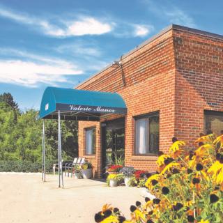 A charming brick building with a blue awning, surrounded by vibrant flowers and a clear sky.