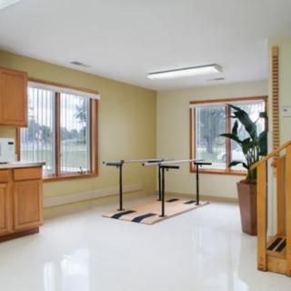 A spacious therapy room equipped with parallel bars and large windows, offering a bright and minimalist environment for rehabilitation exercises.