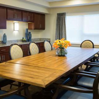 A well-lit conference room with a large wooden meeting table and elegant chairs, featuring decorative vases and a bouquet of flowers.