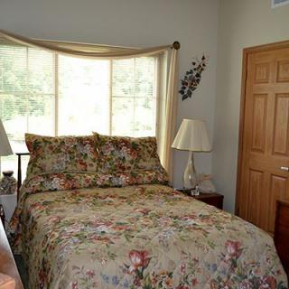 A cozy bedroom with floral bedding, featuring a window with curtains and a lamp on each side.