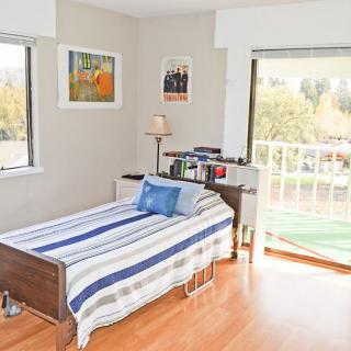A cozy bedroom with a single bed featuring striped bedding, a small bookshelf, and a lamp by the window.