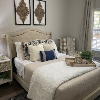 A cozy and elegantly decorated bedroom with a neatly made bed featuring multiple pillows, artwork above the headboard, and a tray placed on the bed.