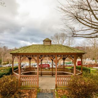 A charming wooden gazebo nestled in a serene park setting, surrounded by nature under a cloudy sky.
