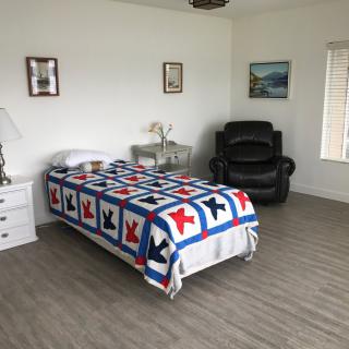 A minimalist bedroom featuring a single bed with a colorful quilt, alongside a black recliner chair.