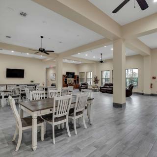 A spacious and well-lit community dining area with modern furnishings and a television.