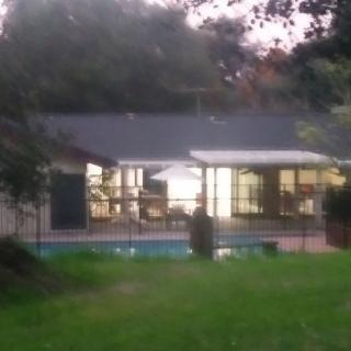 A cozy house with illuminated windows and a pool in the backyard during the evening.