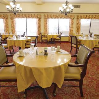 A cozy dining room with elegantly set tables and comfortable chairs, illuminated by classic chandeliers.