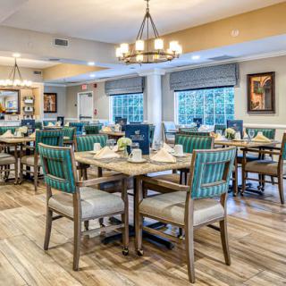 A beautifully decorated dining area with multiple tables and chairs, elegant chandeliers, and large windows offering a pleasant ambiance.