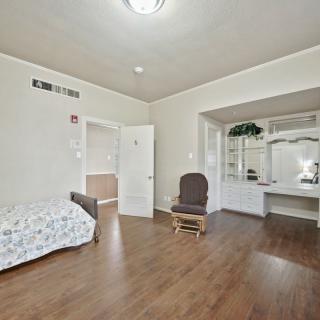 A spacious bedroom with a bed, rocking chair, wooden flooring, and a vanity set with a mirror.