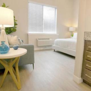 A modern and minimalist bedroom featuring a bed, side table, and large window allowing natural light.