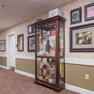 A hallway featuring a glass display case filled with various items, surrounded by framed pictures on the wall.