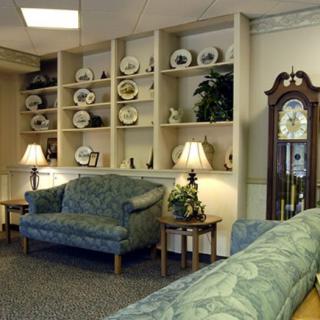 A cozy living room with a couch, lamps, shelves filled with decorative plates, and a grandfather clock.