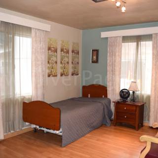 A cozy and well-lit bedroom featuring a single bed, nightstand, and elegant window treatments.