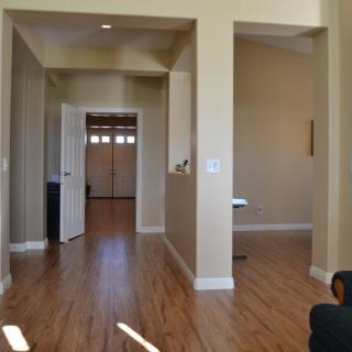 A view of a hallway with wooden flooring and an open door leading to another room.