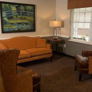 A cozy living room with a sofa, armchairs, a lamp, and a painting on the wall.