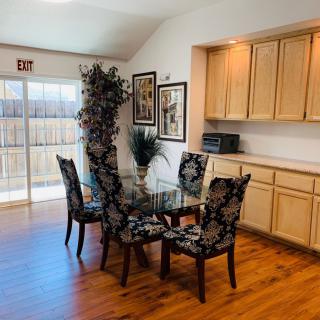 A cozy dining area featuring a glass table with four upholstered chairs, surrounded by warm wood flooring and decorative wall art.