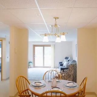 A cozy dining area with a set table, wooden chairs, and a chandelier overhead, illuminated by natural light from a nearby window.
